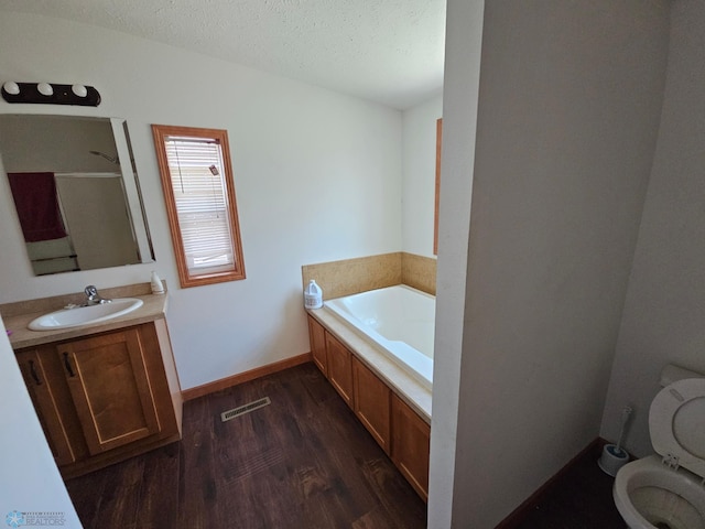 bathroom featuring a textured ceiling, toilet, vanity, a tub to relax in, and hardwood / wood-style floors