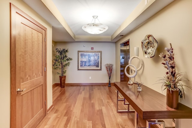 corridor with light hardwood / wood-style floors and a raised ceiling