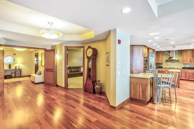 kitchen featuring a breakfast bar area, hardwood / wood-style floors, wall chimney exhaust hood, decorative backsplash, and pendant lighting