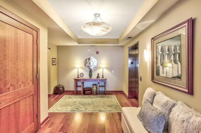 interior space featuring a raised ceiling, elevator, and hardwood / wood-style floors