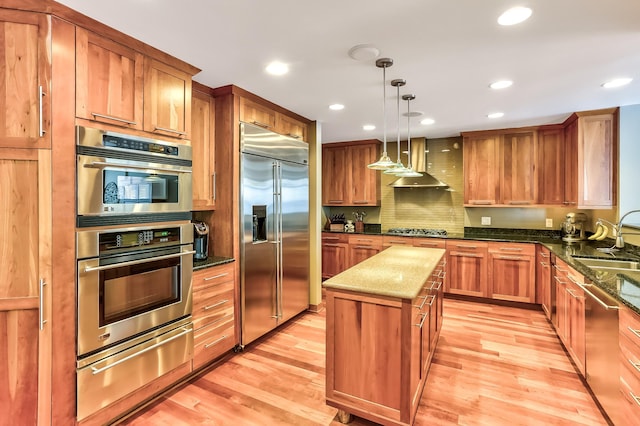 kitchen featuring stainless steel appliances, light hardwood / wood-style flooring, a center island, and wall chimney range hood