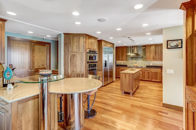 kitchen featuring wall chimney range hood, decorative backsplash, light wood-type flooring, a center island, and appliances with stainless steel finishes