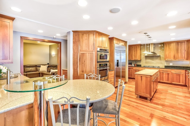 kitchen featuring light hardwood / wood-style flooring, tasteful backsplash, a kitchen island, stainless steel appliances, and wall chimney exhaust hood