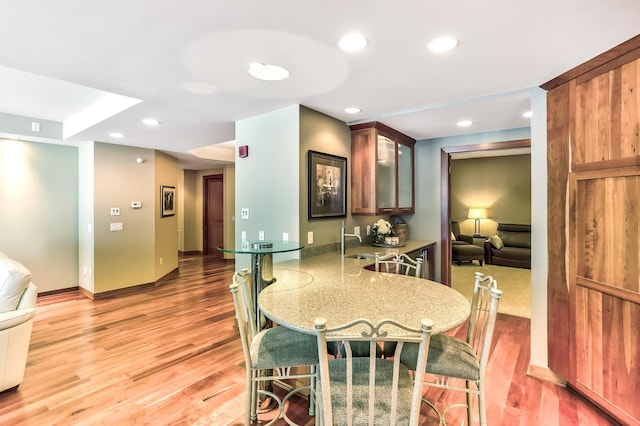 kitchen featuring sink, kitchen peninsula, wood-type flooring, and light stone countertops