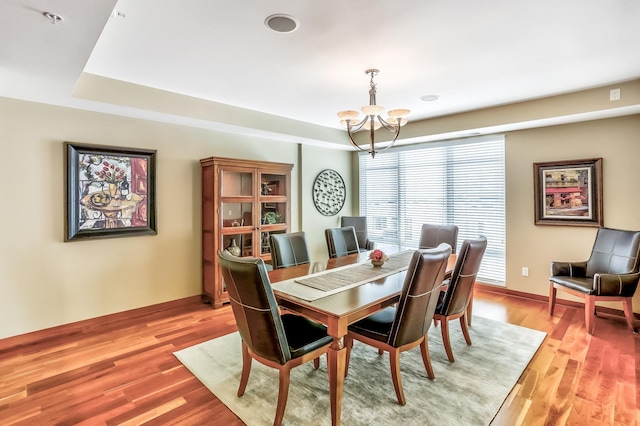 dining space with light hardwood / wood-style flooring, a chandelier, and a tray ceiling