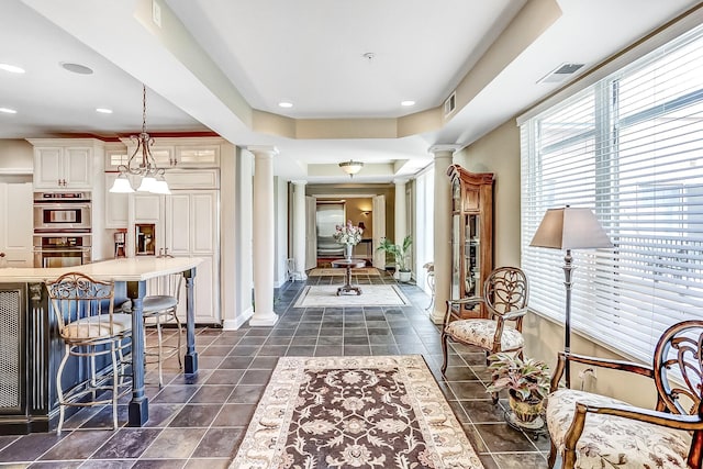 interior space featuring dark tile patterned floors, a raised ceiling, and ornate columns