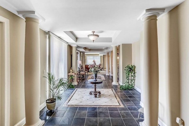 hall with dark tile patterned flooring, a tray ceiling, and ornate columns