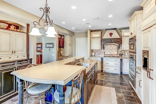 kitchen featuring dark tile patterned floors, tasteful backsplash, premium range hood, an island with sink, and stainless steel appliances