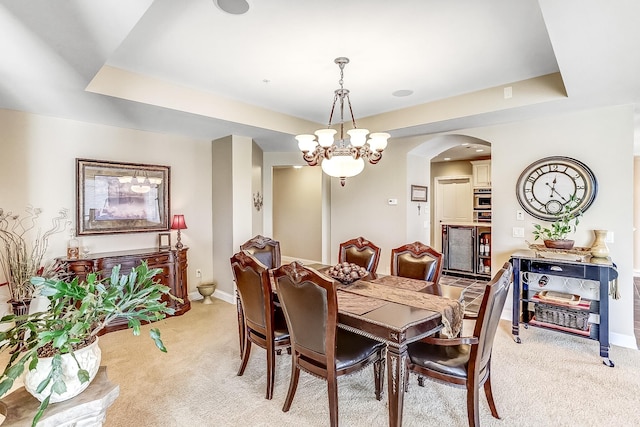 dining room featuring light carpet, a raised ceiling, and a notable chandelier