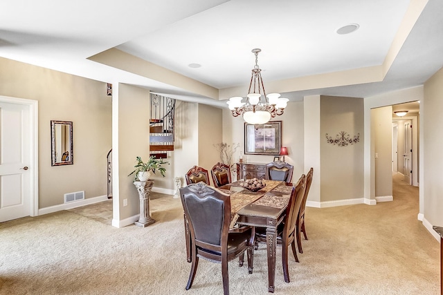 dining space featuring light colored carpet, a raised ceiling, and a chandelier