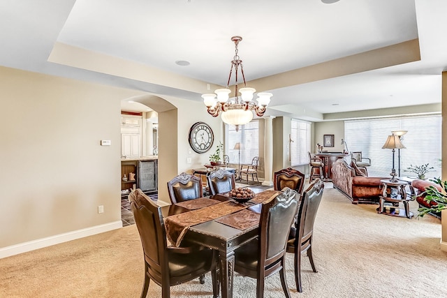 dining space featuring light carpet, a raised ceiling, and a notable chandelier