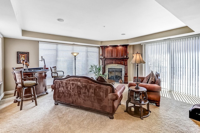 living room with carpet flooring, a raised ceiling, and a tile fireplace