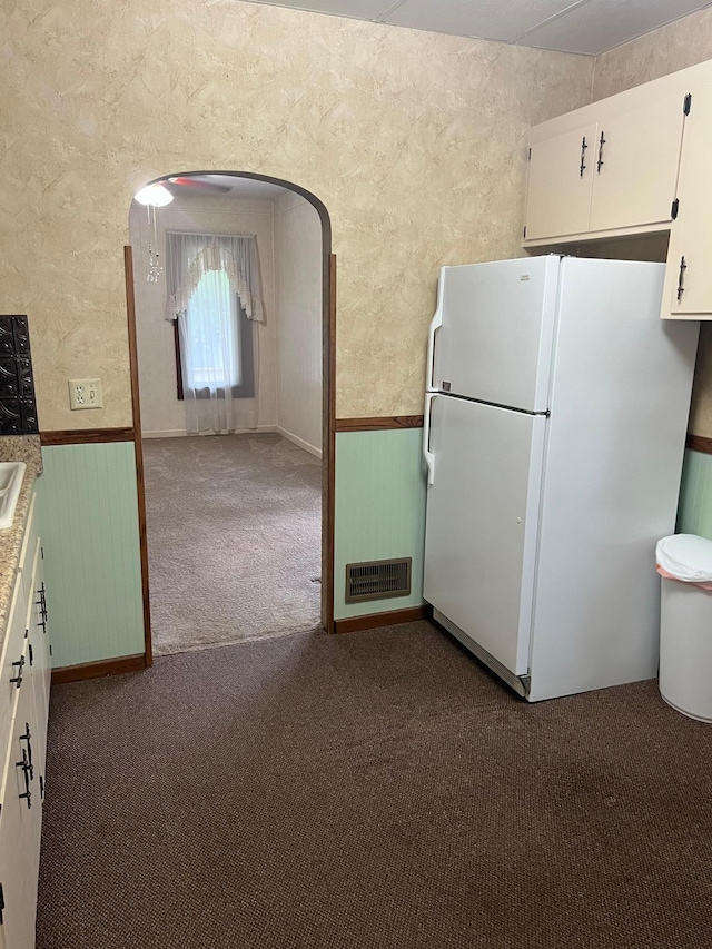 kitchen with dark colored carpet, white fridge, and white cabinetry