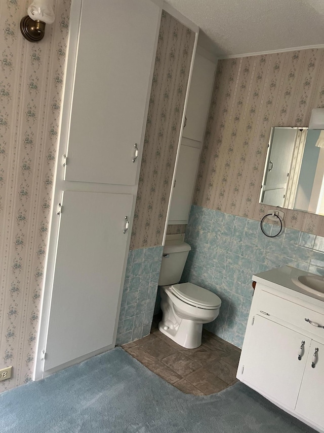 bathroom featuring tile walls, a textured ceiling, tile patterned floors, toilet, and vanity