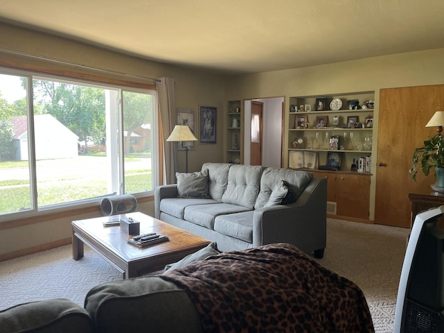 living room featuring light colored carpet, baseboards, visible vents, and built in features