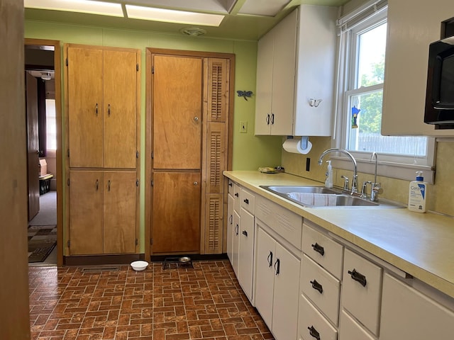 kitchen with a sink, light countertops, a healthy amount of sunlight, and brick patterned floor