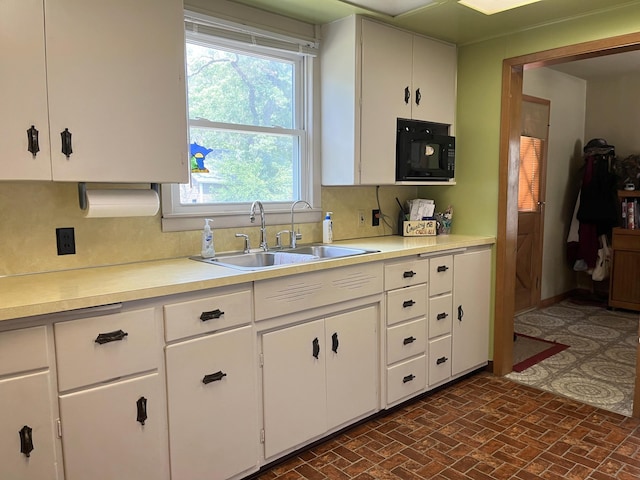 kitchen featuring light countertops, black microwave, decorative backsplash, and a sink