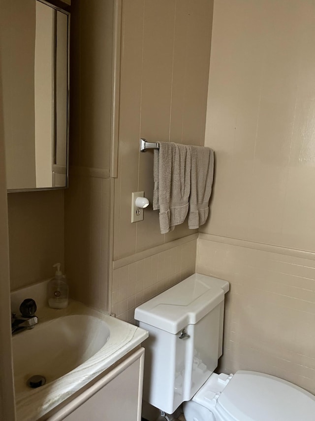 half bathroom featuring a sink, wainscoting, toilet, and tile walls