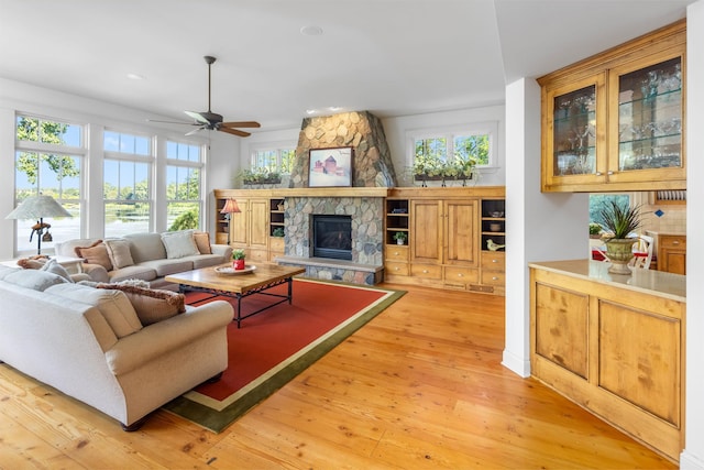 living area with light wood-style flooring, a fireplace, a wealth of natural light, and a ceiling fan