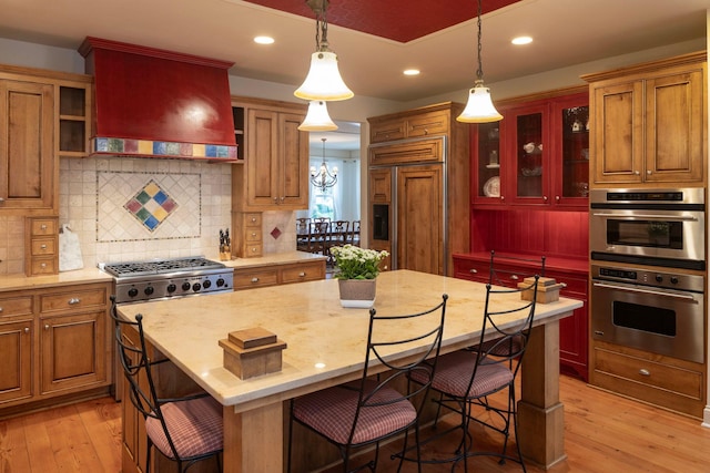 kitchen featuring paneled built in fridge, light wood finished floors, premium range hood, and stainless steel double oven