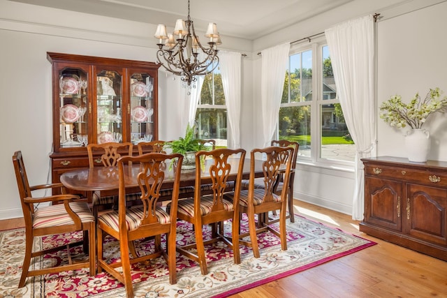 dining room featuring light wood-type flooring, a healthy amount of sunlight, a notable chandelier, and baseboards