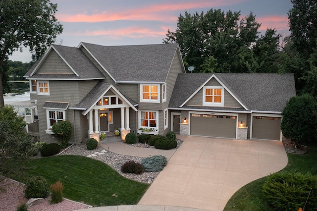 craftsman-style house with a shingled roof, concrete driveway, stone siding, an attached garage, and a front lawn