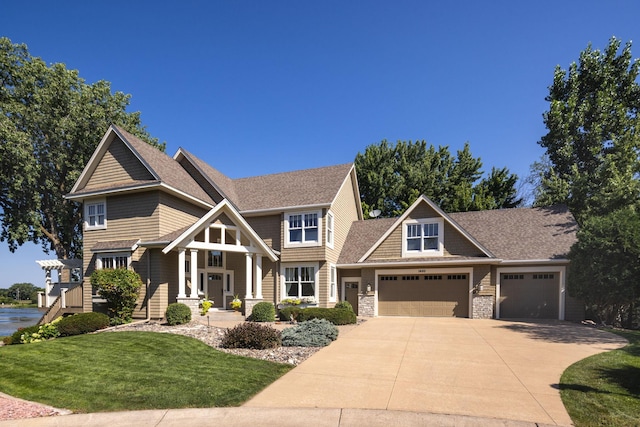 view of front facade with a shingled roof, concrete driveway, a front yard, a garage, and stone siding