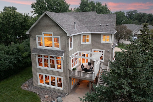 back of property at dusk featuring a yard, a shingled roof, stairway, and a wooden deck