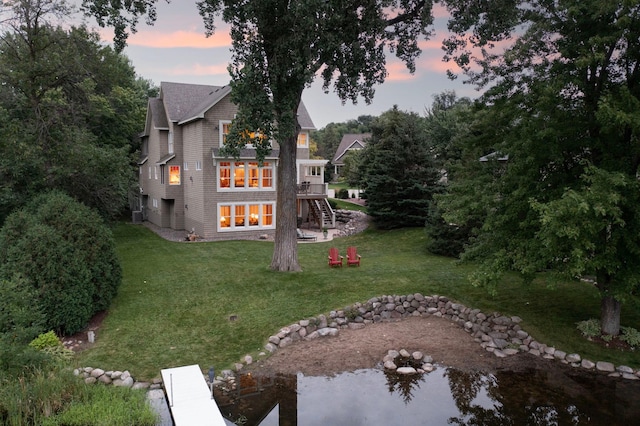 back house at dusk featuring a lawn