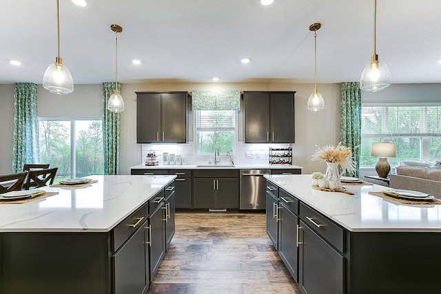 kitchen with light wood-type flooring, backsplash, stainless steel dishwasher, sink, and hanging light fixtures