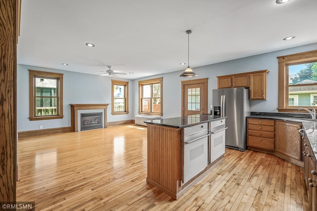 kitchen with radiator heating unit, light hardwood / wood-style floors, stainless steel fridge, decorative light fixtures, and oven