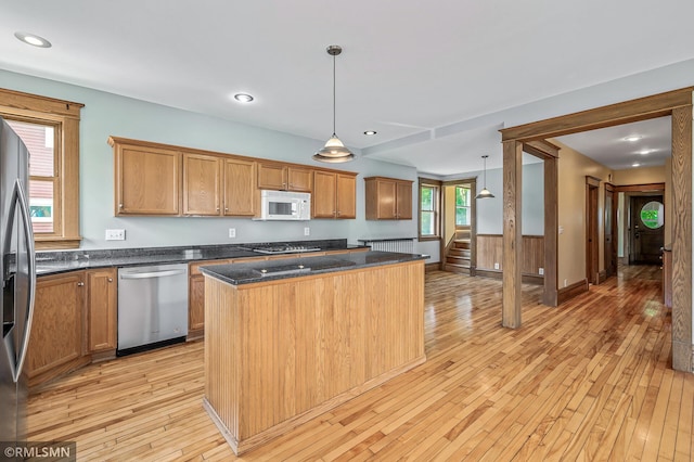 kitchen featuring stainless steel appliances, decorative light fixtures, light wood-type flooring, dark stone countertops, and a center island