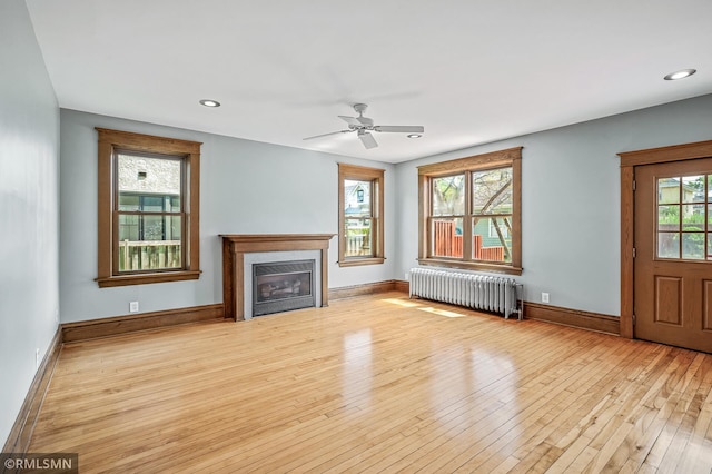 unfurnished living room featuring radiator heating unit, light hardwood / wood-style floors, and ceiling fan