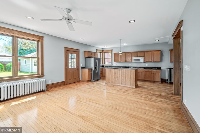 kitchen featuring decorative light fixtures, radiator heating unit, stainless steel refrigerator with ice dispenser, a kitchen island, and light hardwood / wood-style floors