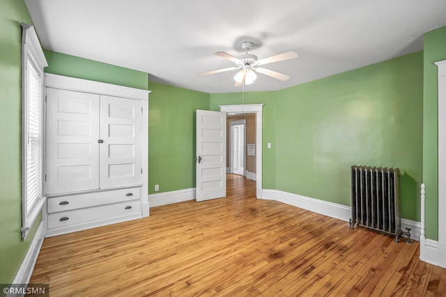 unfurnished bedroom with radiator heating unit, ceiling fan, light hardwood / wood-style flooring, and a closet