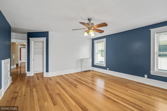 spare room featuring radiator, light hardwood / wood-style flooring, a healthy amount of sunlight, and ceiling fan