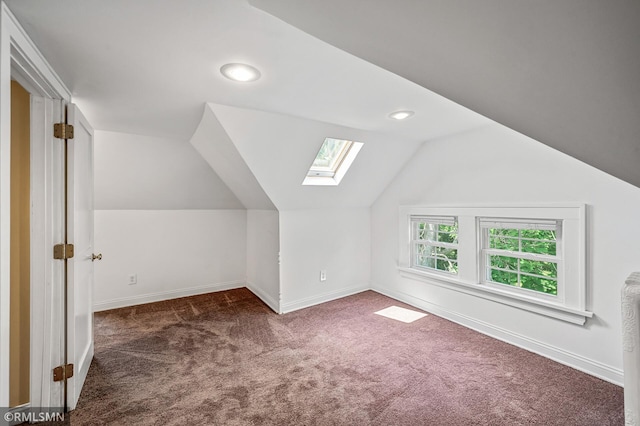 bonus room with dark colored carpet and vaulted ceiling with skylight