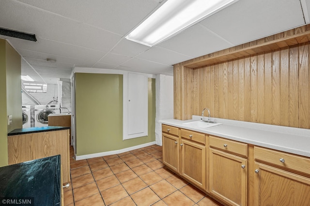 kitchen featuring light tile patterned flooring, independent washer and dryer, wooden walls, and sink