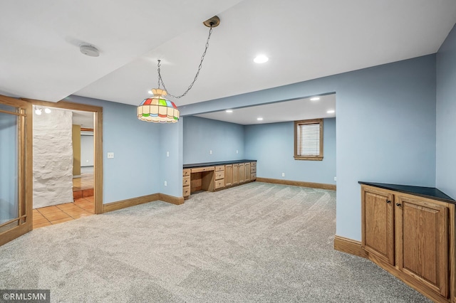 kitchen with pendant lighting, light colored carpet, and built in desk