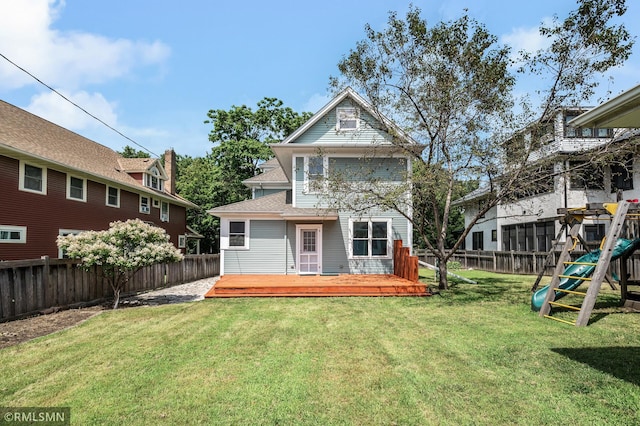 rear view of house with a wooden deck, a yard, and a playground