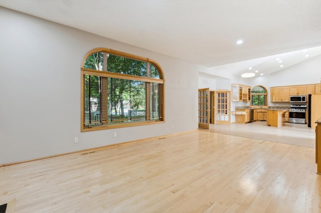 unfurnished living room with vaulted ceiling, light hardwood / wood-style floors, and french doors