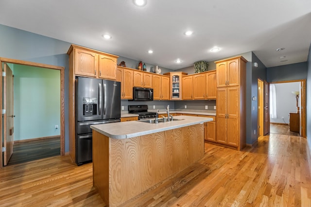 kitchen with stainless steel refrigerator with ice dispenser, sink, gas range oven, a center island with sink, and light hardwood / wood-style flooring