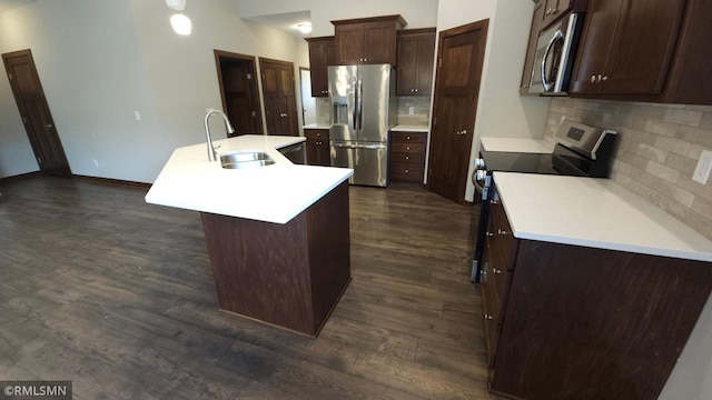 kitchen with stainless steel appliances, a center island with sink, sink, decorative backsplash, and dark hardwood / wood-style floors