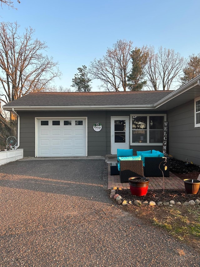 ranch-style house featuring a garage, driveway, outdoor lounge area, and a shingled roof