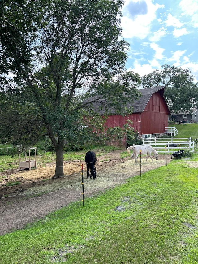 view of yard featuring a barn, a rural view, fence, and an outdoor structure