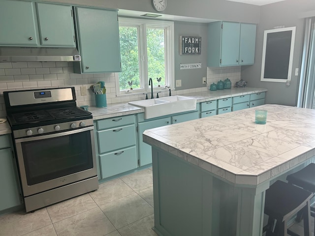 kitchen featuring decorative backsplash, stainless steel range with gas stovetop, light countertops, under cabinet range hood, and a sink