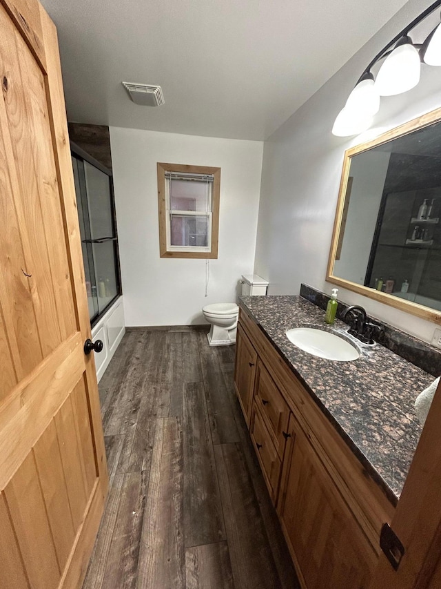 bathroom with toilet, bath / shower combo with glass door, wood finished floors, vanity, and visible vents