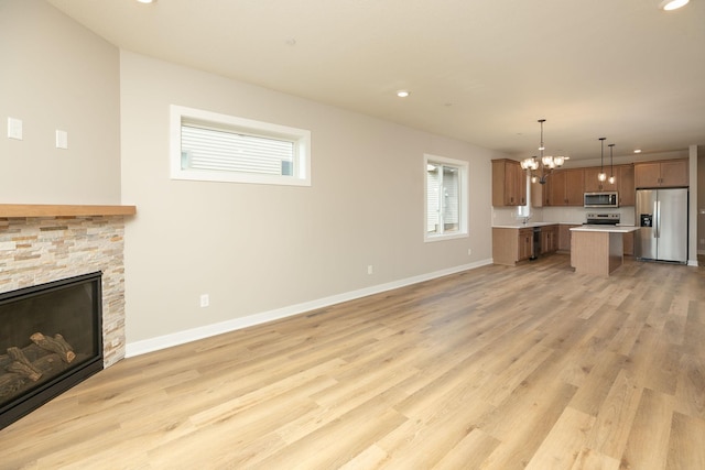 unfurnished living room featuring a chandelier, light hardwood / wood-style flooring, and a stone fireplace