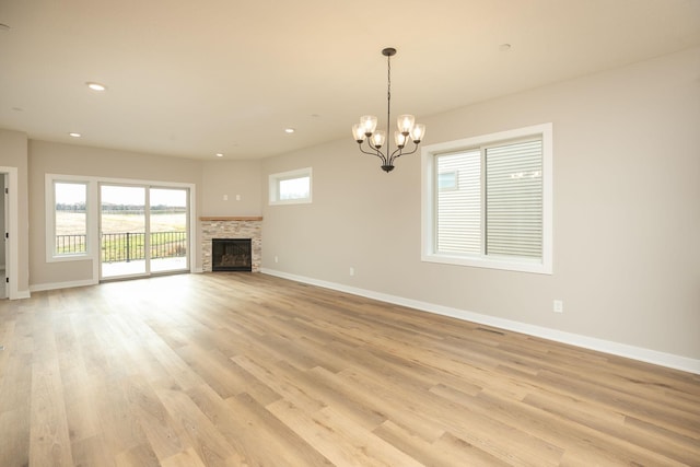 unfurnished living room with a notable chandelier, light hardwood / wood-style floors, and a stone fireplace