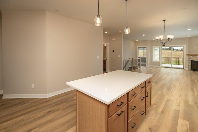 kitchen with light wood-type flooring, pendant lighting, a stone fireplace, a notable chandelier, and a center island